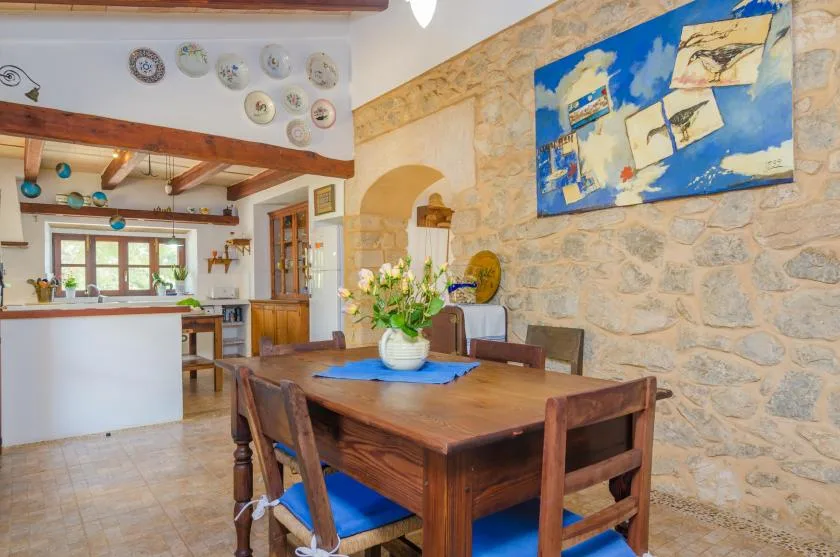 Comedor con una mesa de madera, un cuadro colorido y una cocina contigua.
