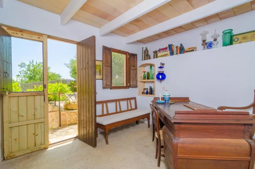Una habitación luminosa con mesa de madera, asientos tipo banco y una puerta abierta al jardín.