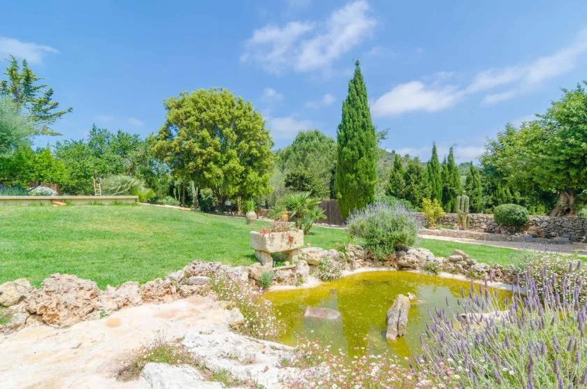 Un jardín paisajístico con un pequeño estanque, césped y plantas con flores.