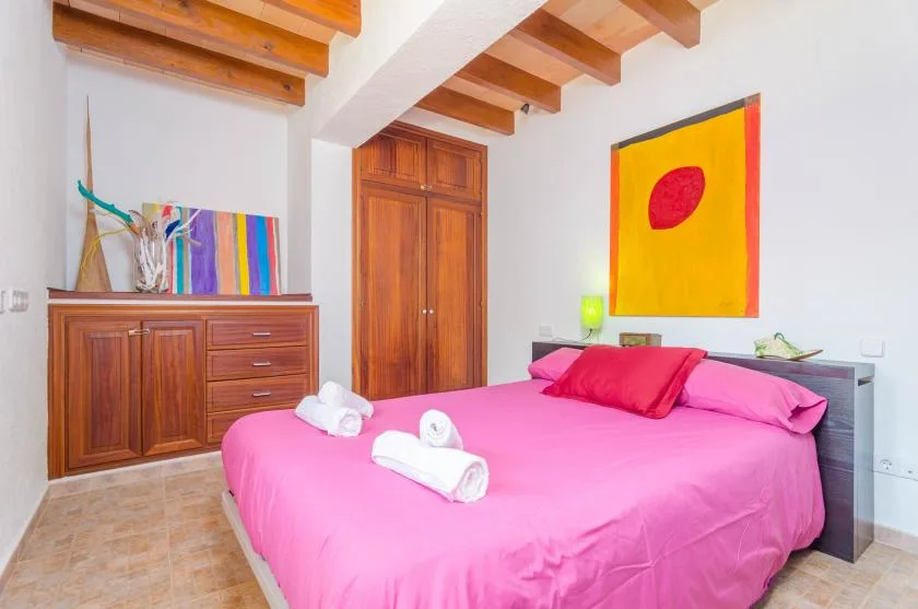 Un dormitorio con una cama de color rosa intenso y una obra colorida en la pared.