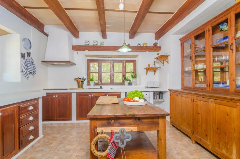 Una cocina luminosa con armarios de madera, vigas expuestas y una mesa de trabajo central.