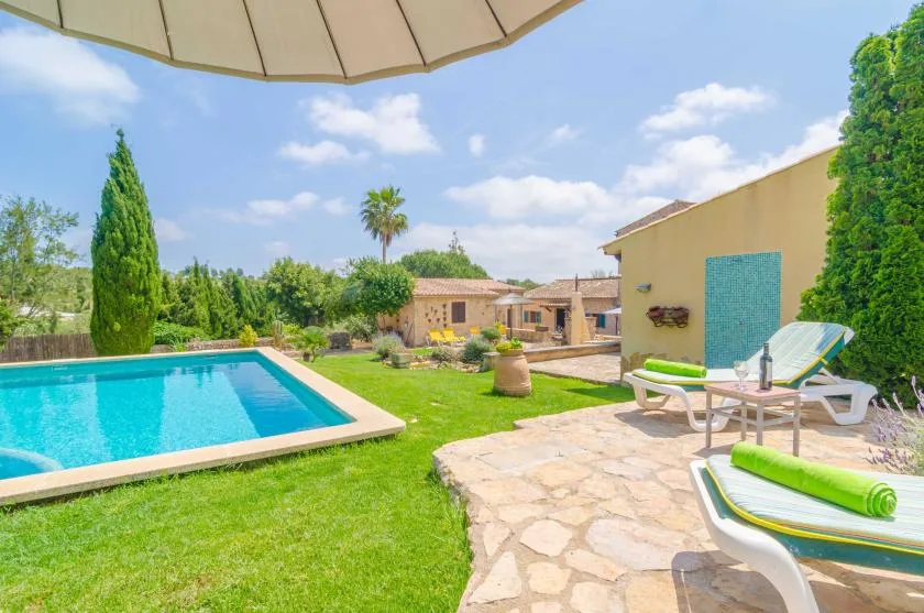 Un jardín soleado con piscina, patio de piedra y asientos al aire libre.