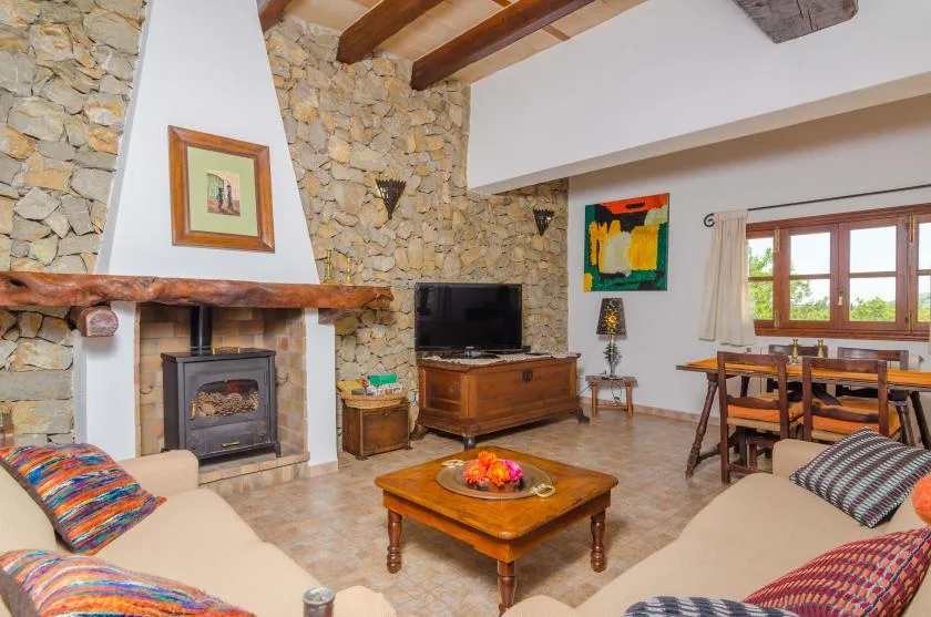Un salón-comedor con chimenea de piedra, muebles de madera y ventanas grandes.