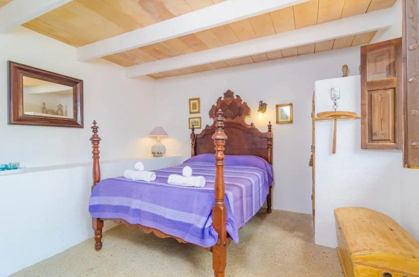 Un dormitorio con una cama de madera vestida con ropa de cama morada y toallas dobladas.