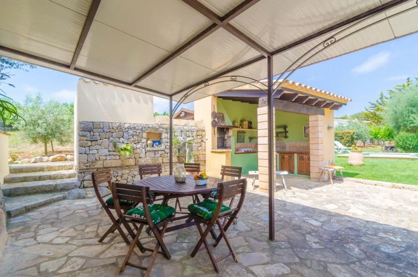 Un patio de piedra cubierto tiene una mesa de madera junto a una cocina exterior.