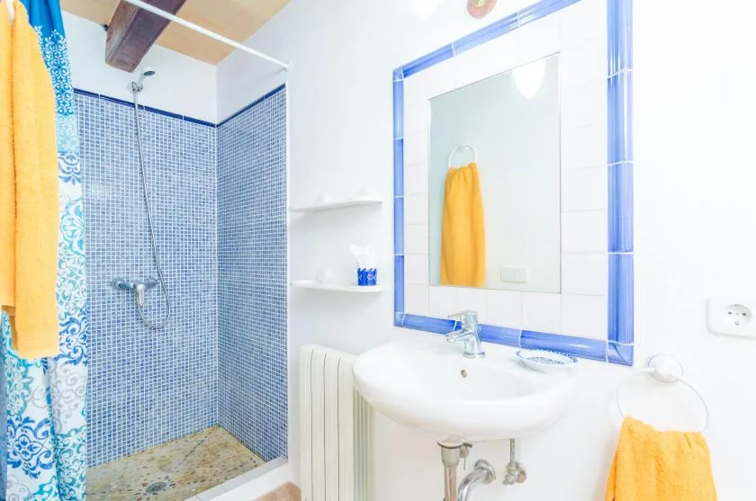 Un baño luminoso con lavabo, espejo y zona de ducha alicatada.