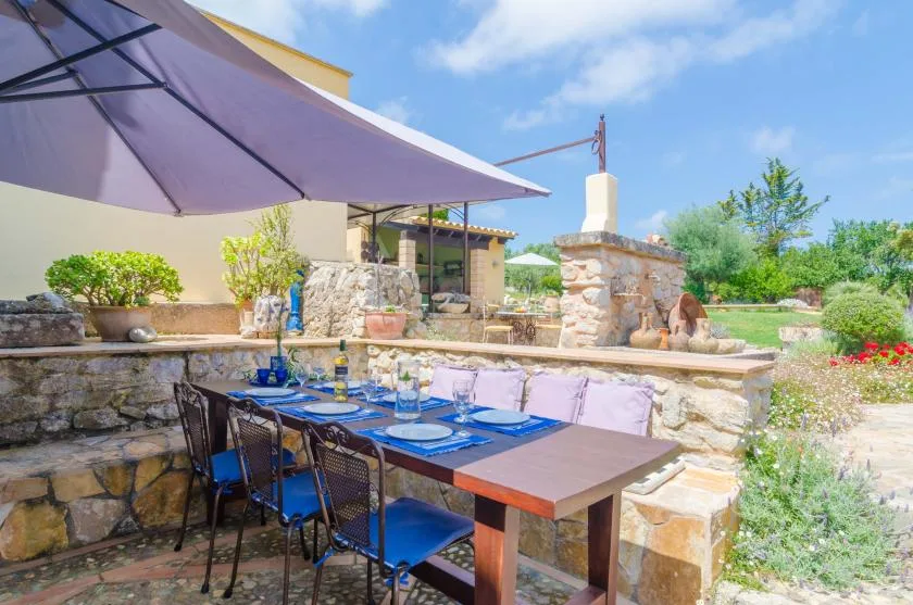 Un comedor al aire libre con una mesa a la sombra junto a un muro de piedra.