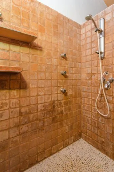 Una ducha con azulejos, controles en la pared y un cabezal de mano.