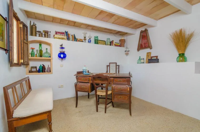 Una habitación amueblada con escritorio de madera, sillas y estantes con objetos decorativos.