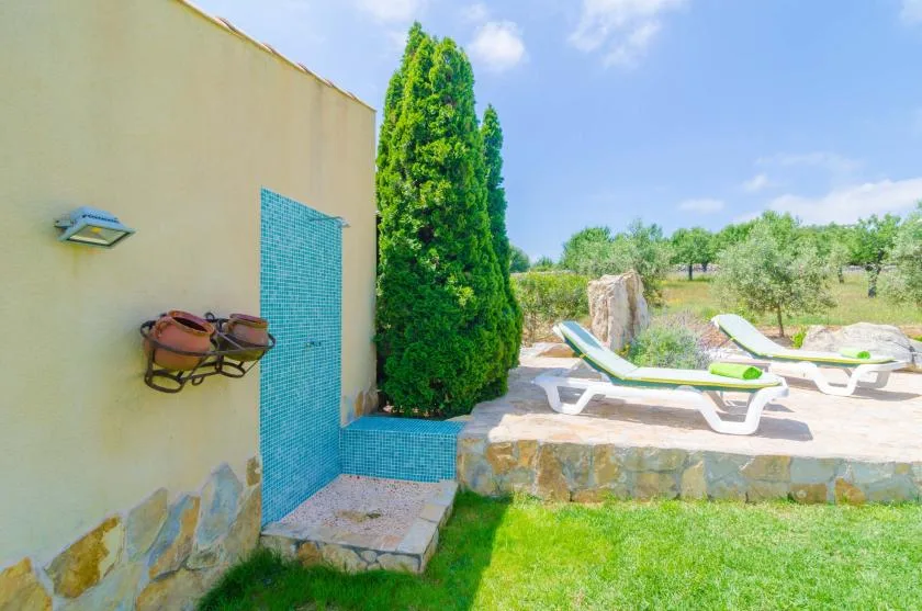 Un patio junto a la piscina con tumbonas junto a una pared de ducha con azulejos.