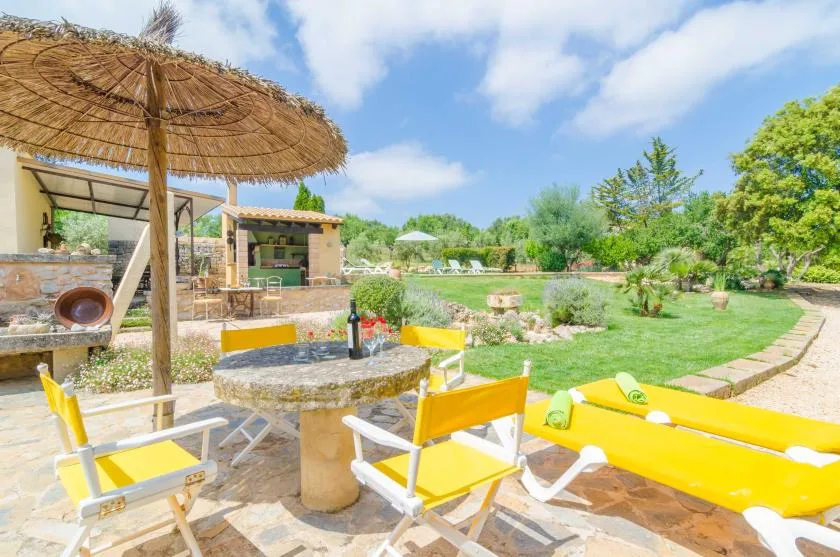 Un patio soleado con asientos amarillos, una mesa redonda y una sombrilla de paja.