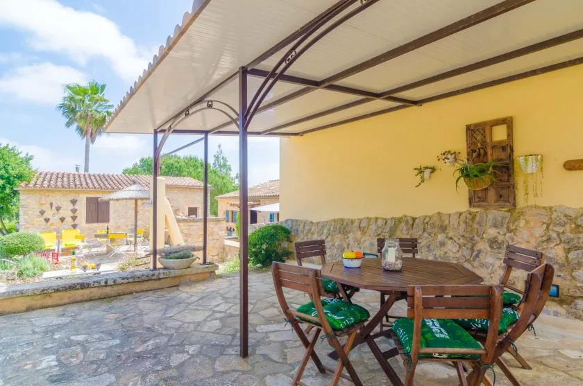 Un comedor exterior cubierto con una mesa de madera y asientos con cojines verdes.
