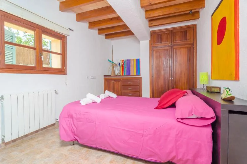 Un dormitorio con una cama rosa intenso bajo vigas de madera a la vista.
