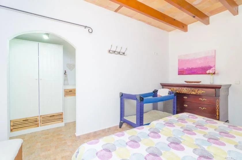Un dormitorio con una cama colorida, una cómoda de madera y una cuna azul.