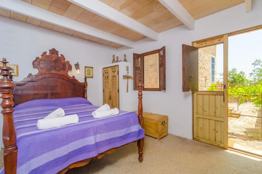 Un dormitorio con una cama de madera vestida con ropa de cama morada junto a una puerta abierta.