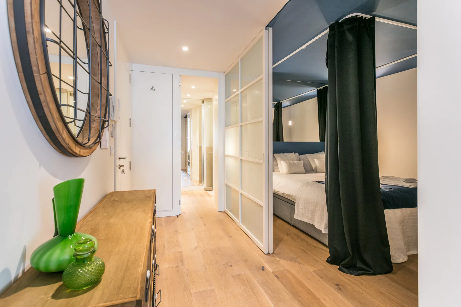 Un dormitorio con una cama tras una cortina oscura y un pasillo al fondo.