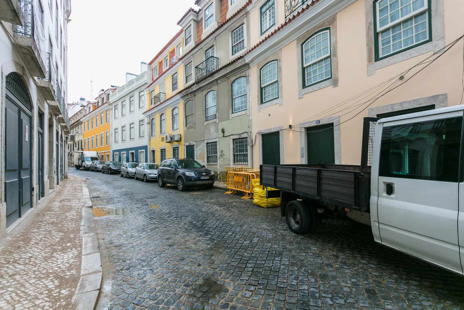 Una calle empedrada bordeada de edificios coloridos y vehículos estacionados.