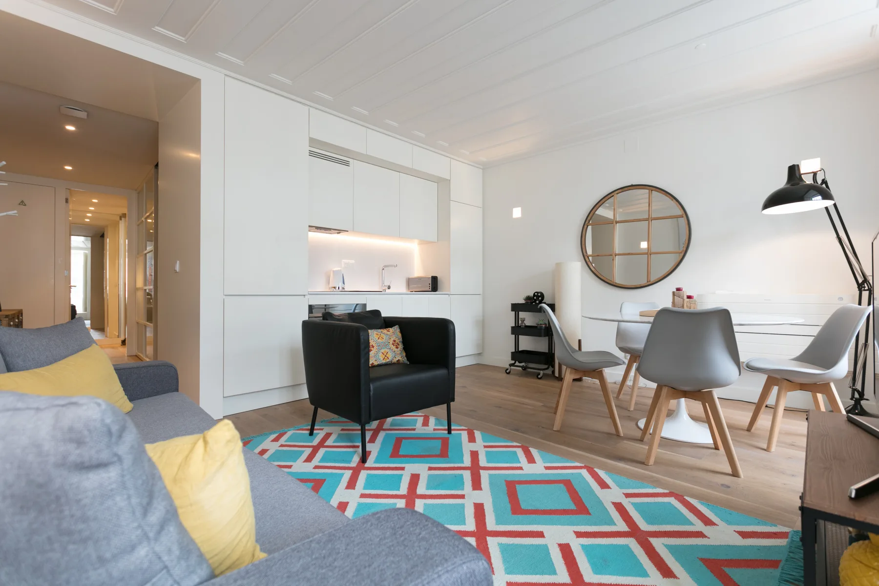Una sala luminosa con asientos, una mesa de comedor y una alfombra de colores.