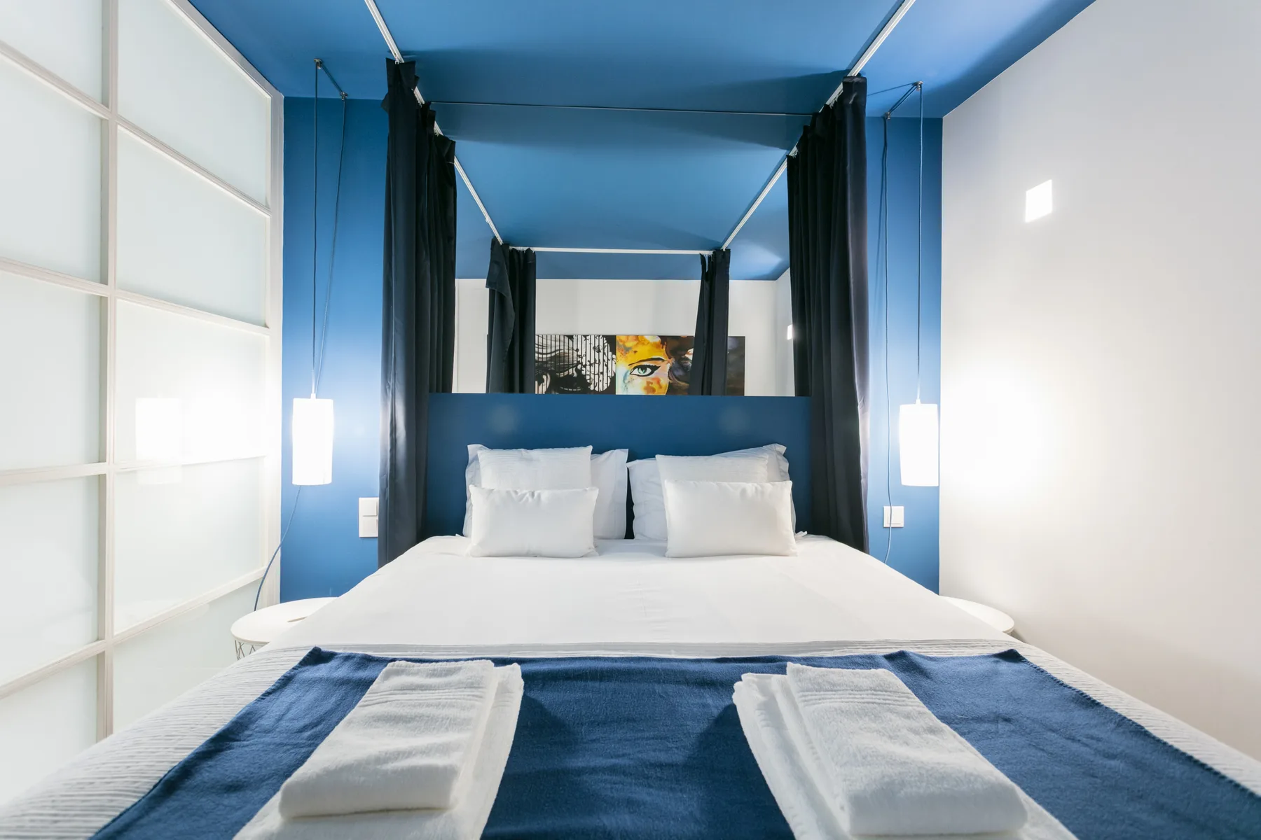 Un dormitorio con una cama, ropa de cama blanca y paredes azules.