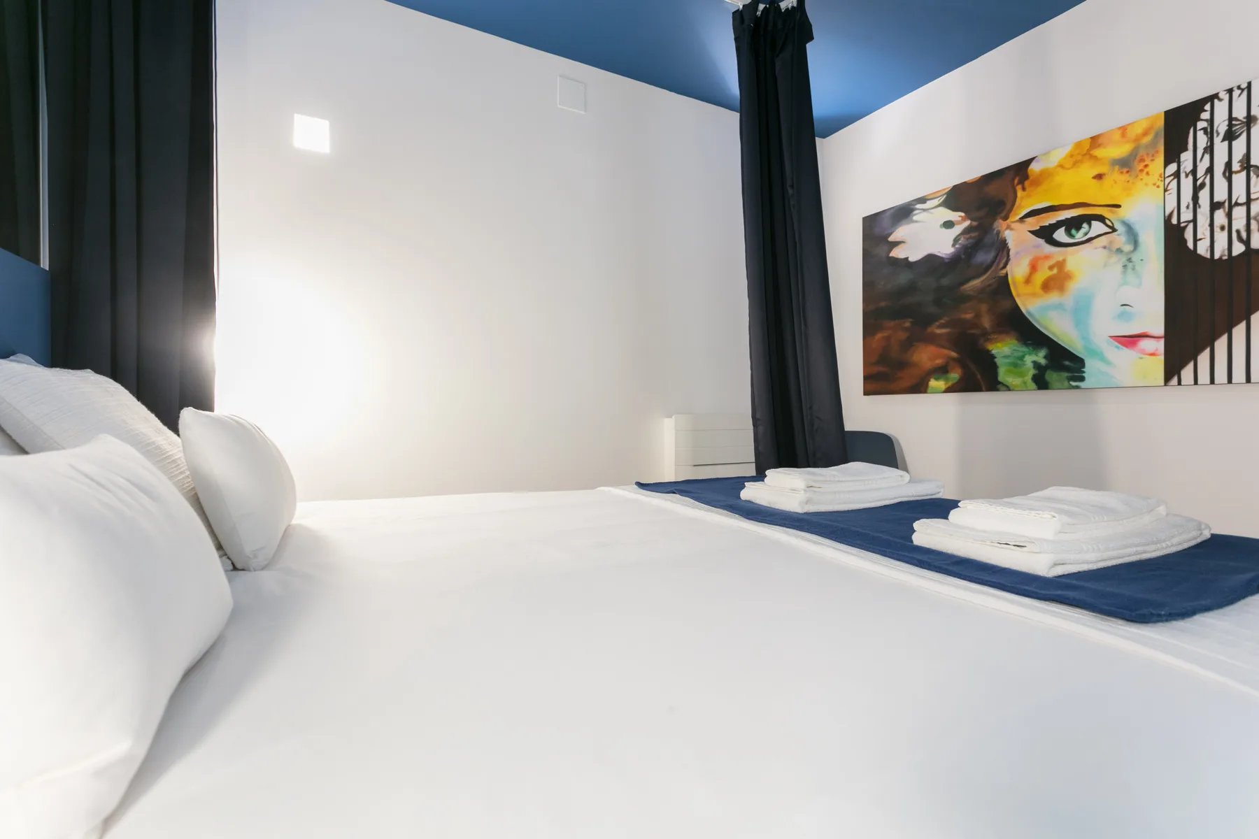 Un dormitorio con ropa de cama blanca y una obra colorida en la pared.