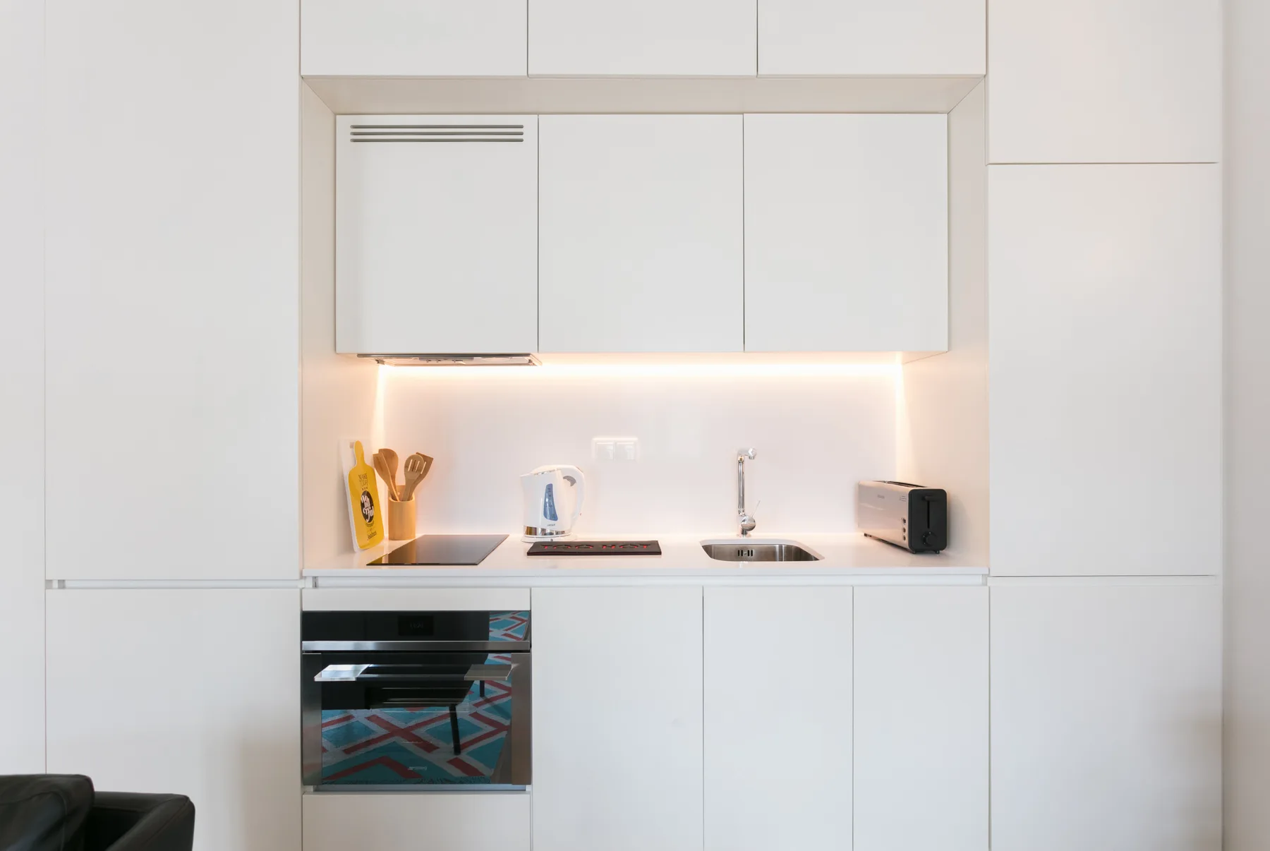 Una cocina compacta con gabinetes blancos, una placa de cocción y un horno.