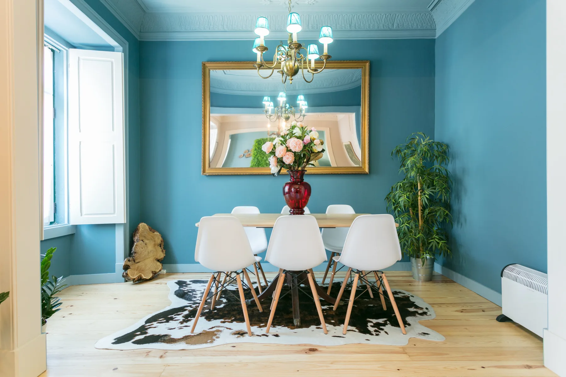 Un comedor azul con una mesa, sillas y un gran espejo en la pared.