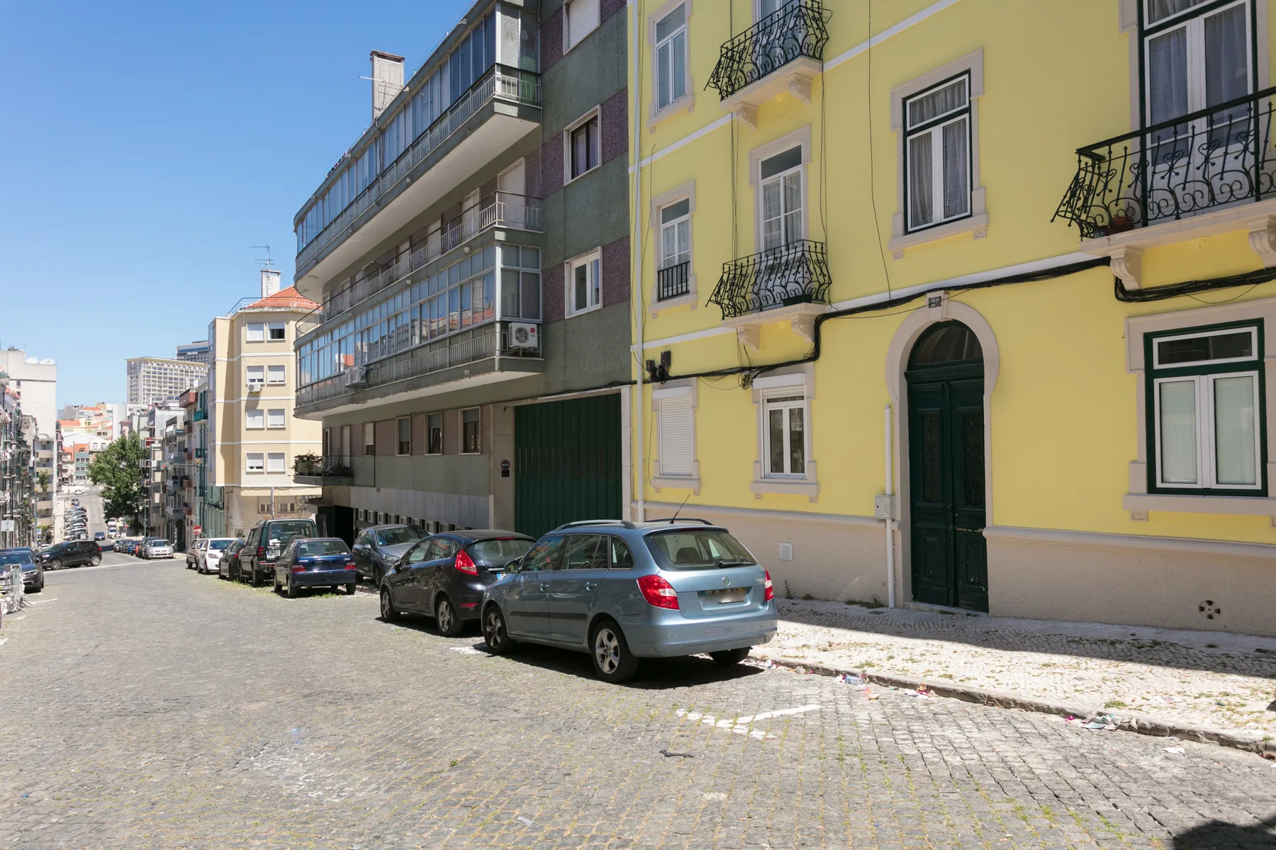 Una calle empedrada bordeada de coches estacionados y edificios de apartamentos coloridos.