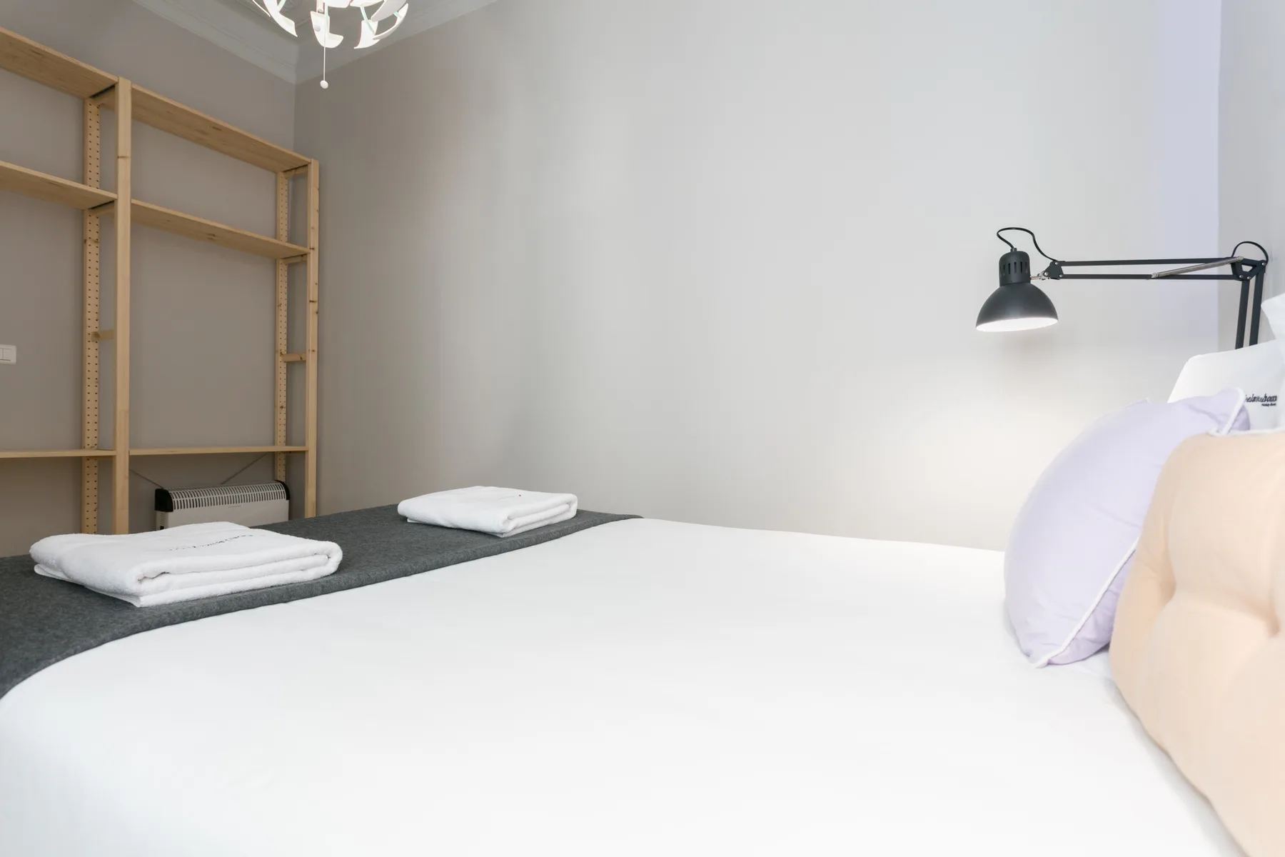 A bedroom with a large bed, folded towels, and open shelving.