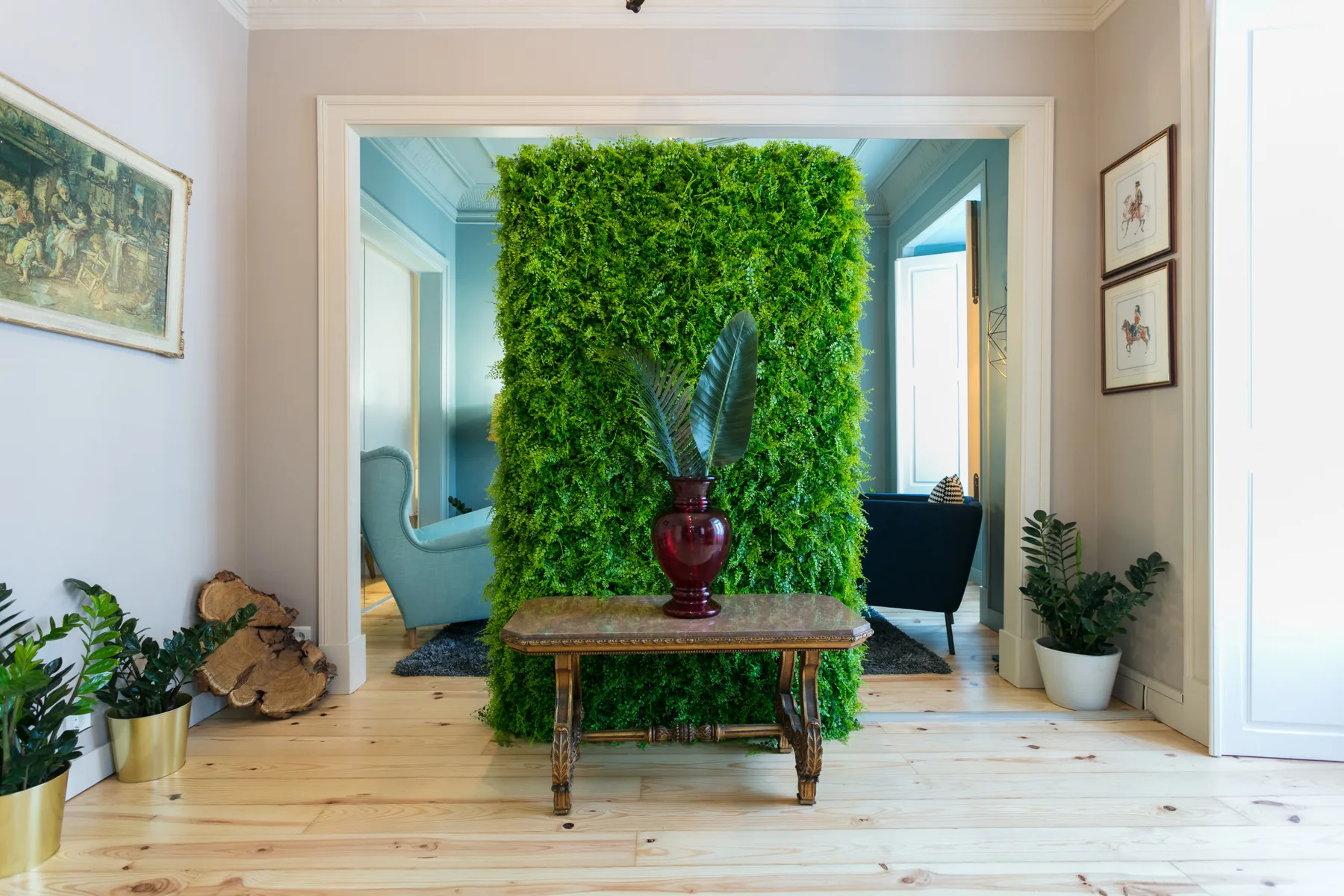 Un pasillo interior luminoso presenta una pared verde frondosa y una pequeña mesa de madera.
