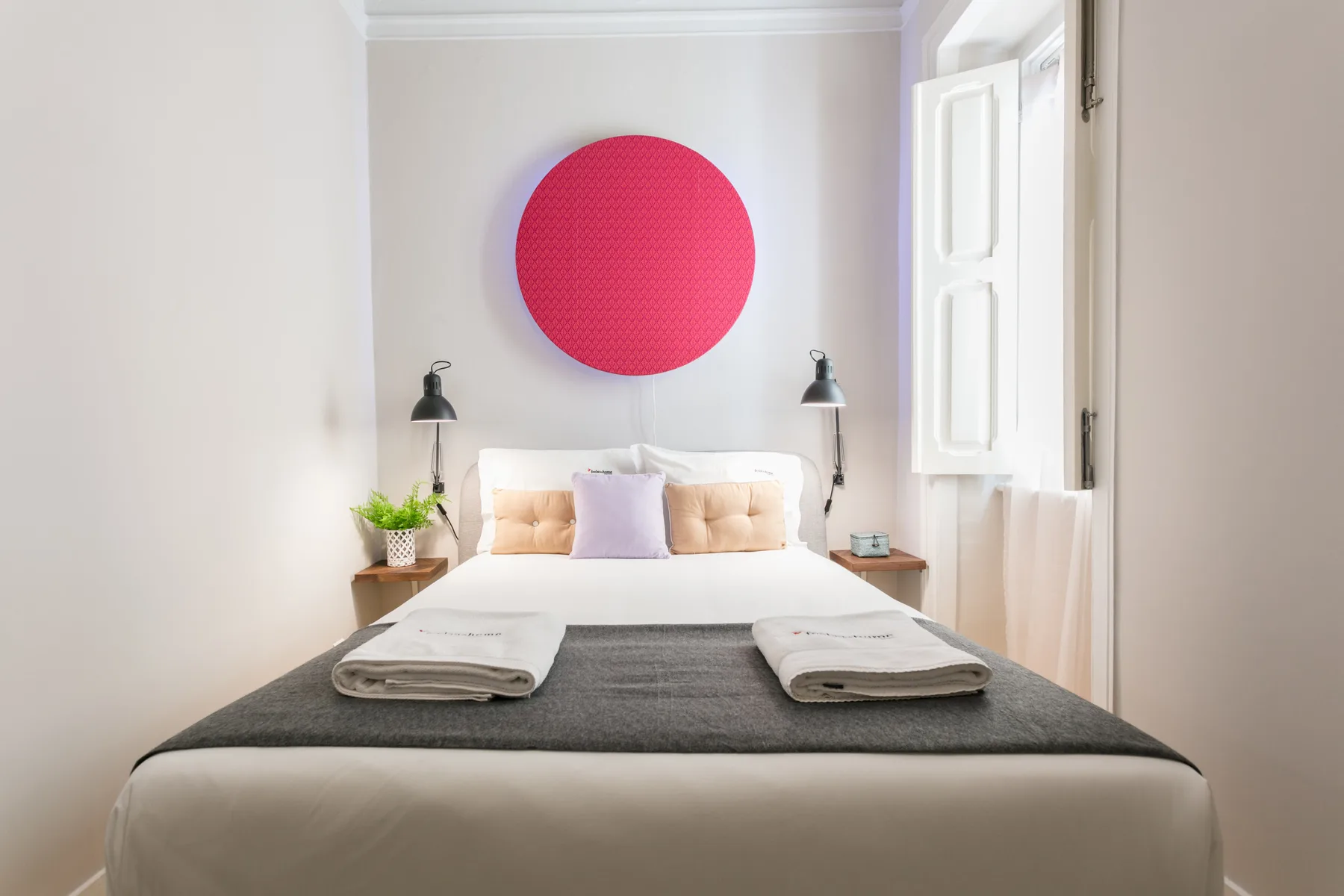 A bright bedroom with a bed and a large circular wall decoration.