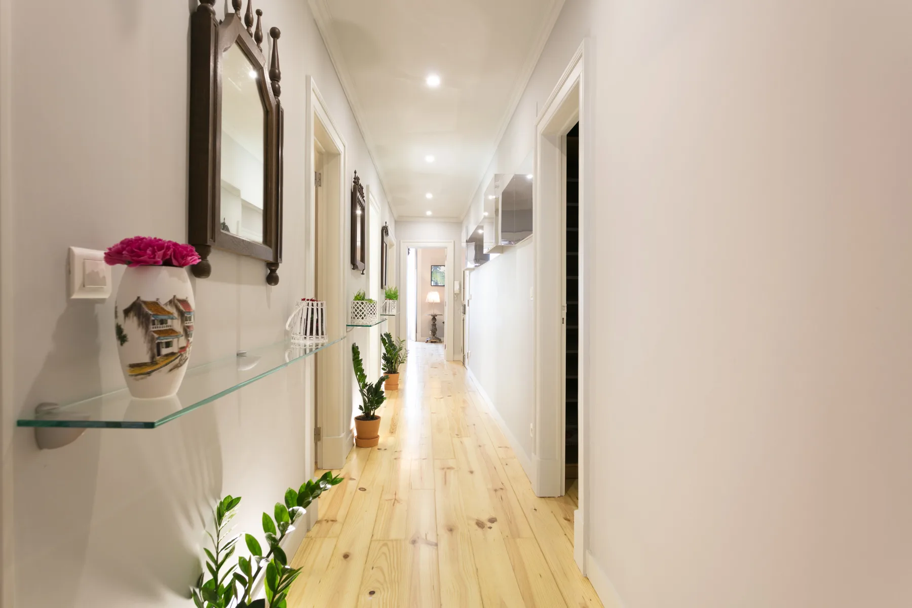Un pasillo luminoso con suelo de madera clara y espejos en la pared.