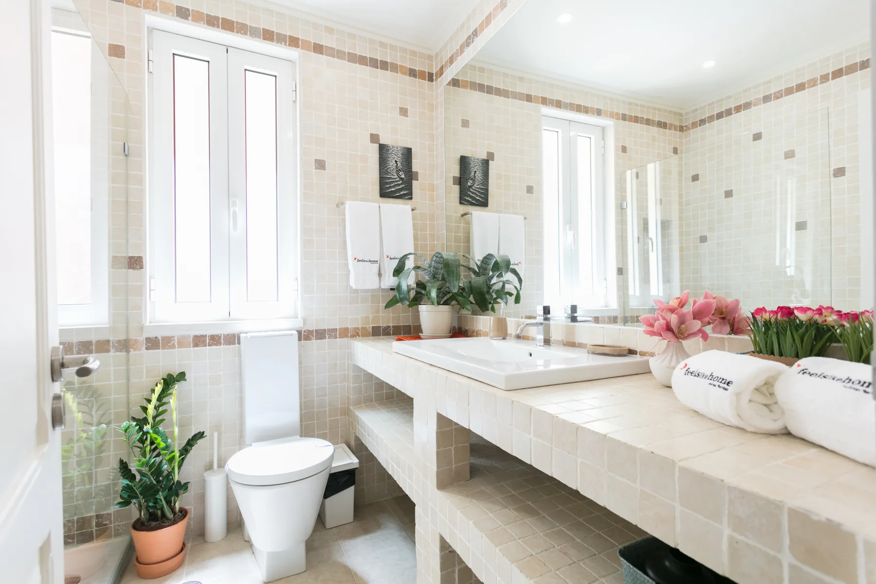 Un baño alicatado con inodoro, lavabo y arreglos florales.