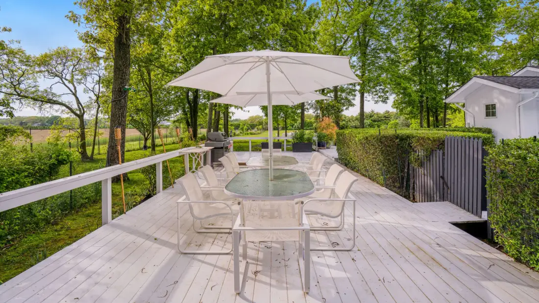 Una zona de comedor al aire libre en una terraza de madera, protegida por una gran sombrilla.