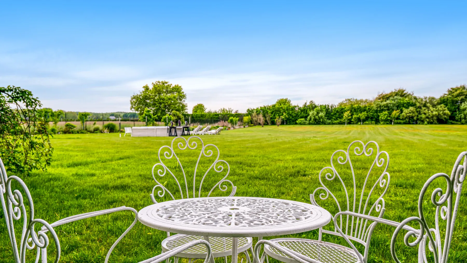 Un conjunto de comedor al aire libre da a un amplio césped verde y una línea de árboles.