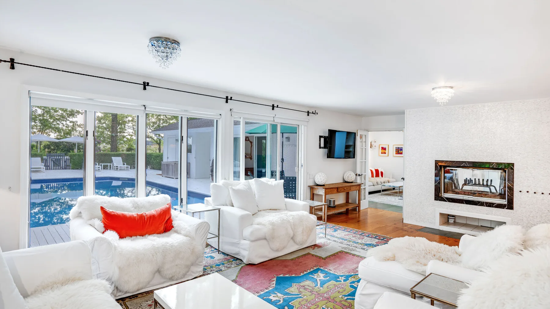 Una sala luminosa con asientos blancos, alfombras coloridas y puertas de vidrio que dan a una piscina.