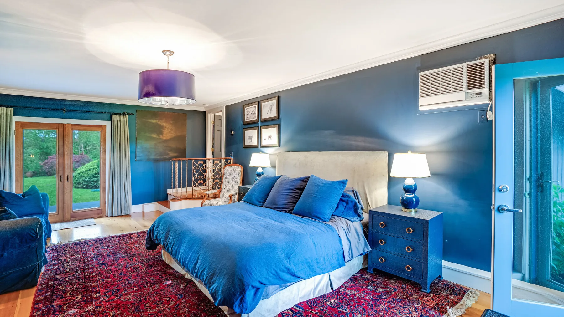 Un dormitorio con una cama azul, una mesita de noche y puertas de vidrio hacia un patio.