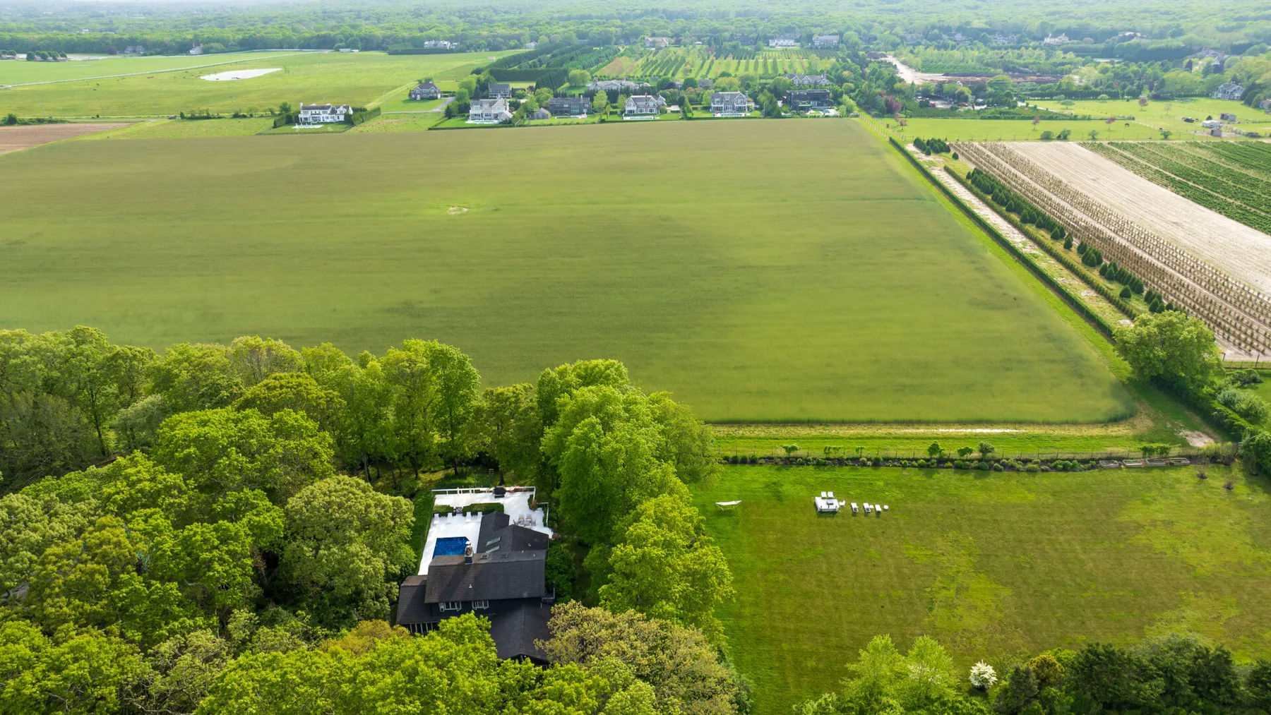 Vista aérea de extensos campos verdes, con árboles y edificios dispersos.