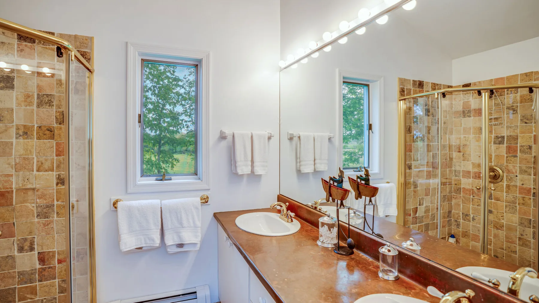 Un baño luminoso con un tocador largo, espejos y una ducha revestida de azulejos.