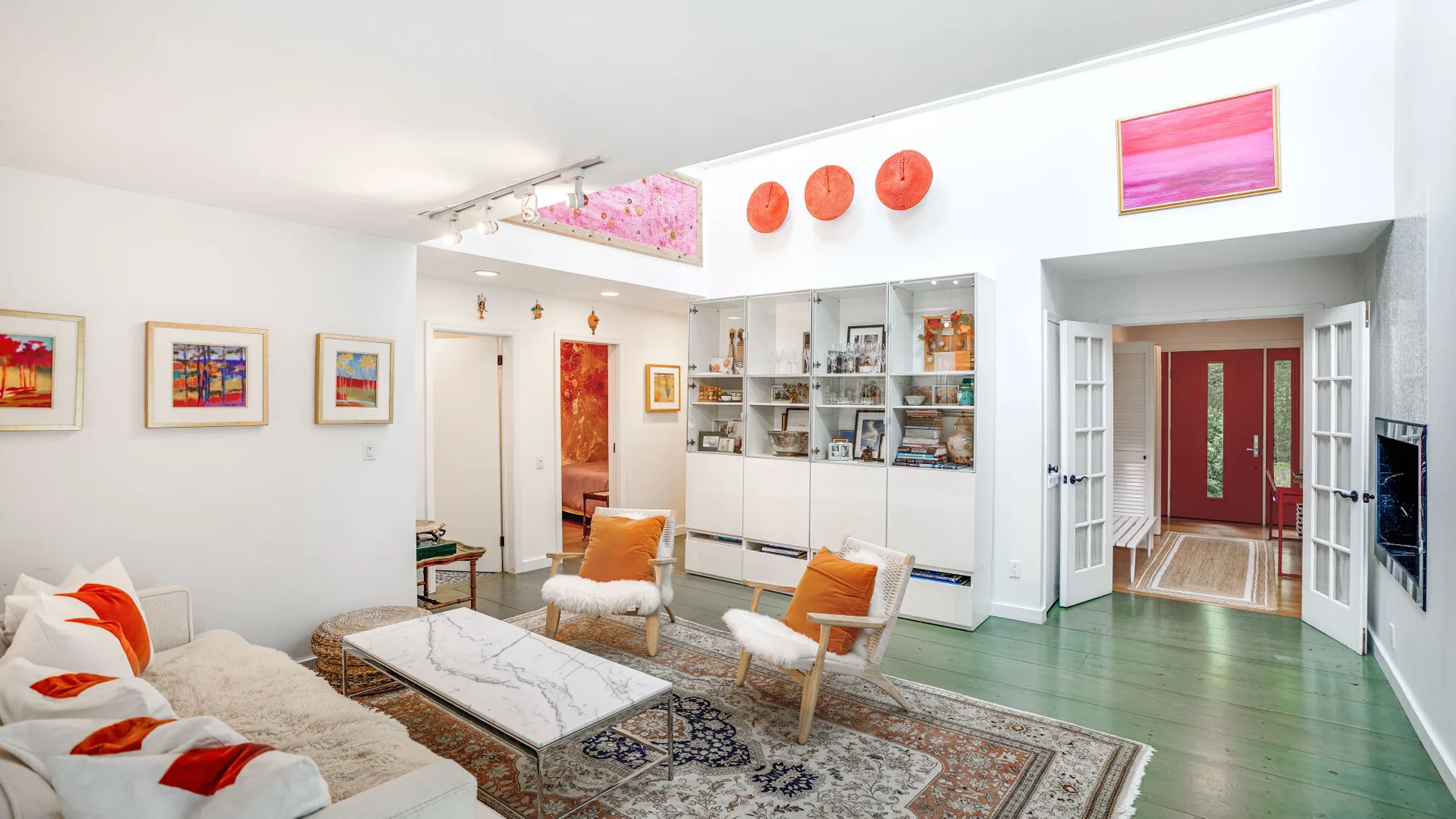 Una sala luminosa tiene obras de arte coloridas, asientos y una mesa de centro con superficie de vidrio.
