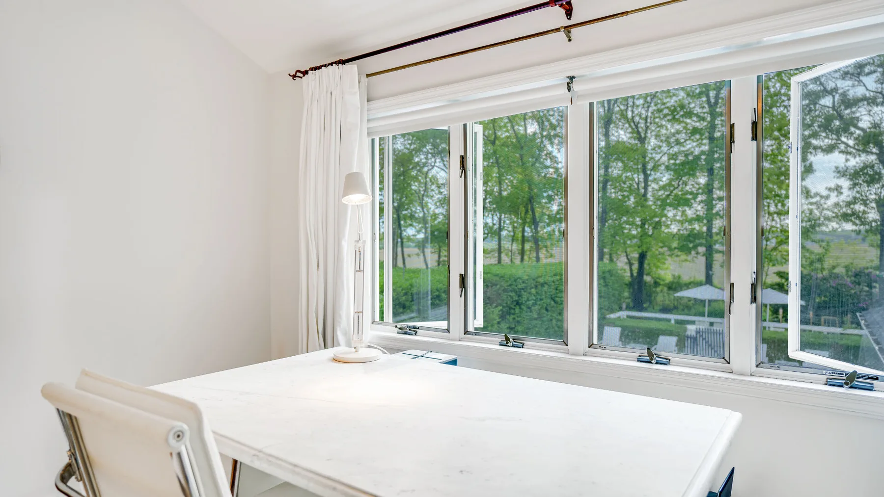 Un comedor luminoso con una mesa blanca junto a grandes ventanas con vista a los árboles.