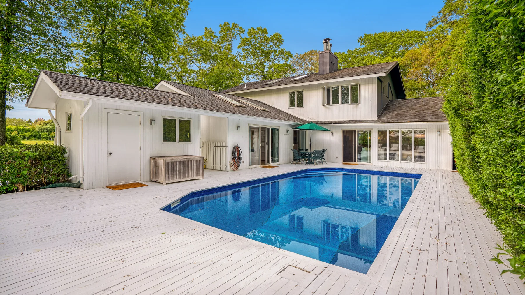 Una piscina está junto a una casa blanca, rodeada por una amplia terraza de madera.