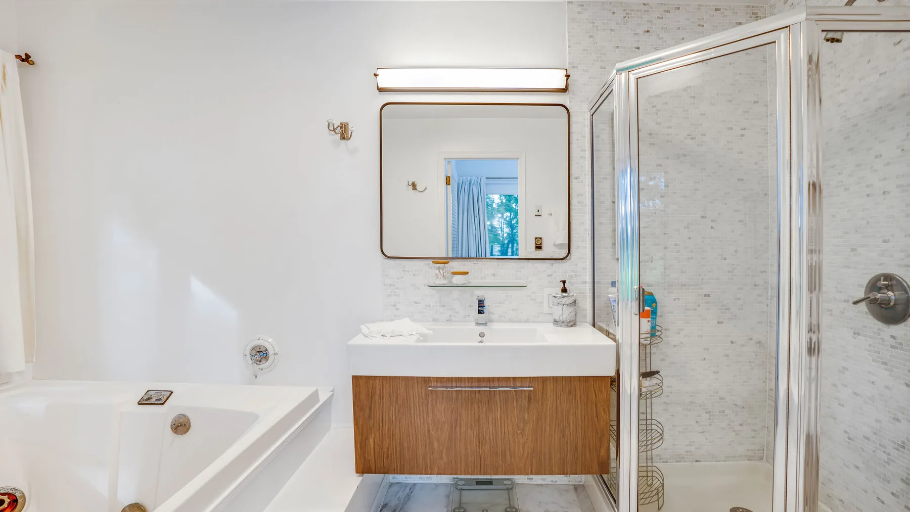 Un baño luminoso con bañera, lavabo y ducha con mampara de vidrio.