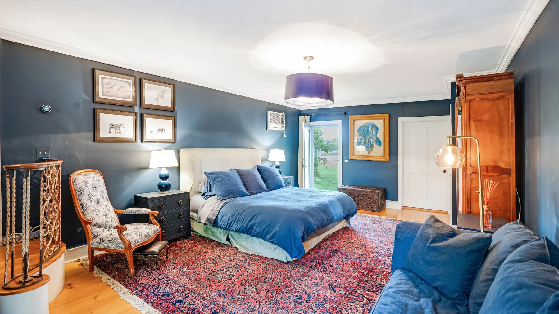 Un dormitorio con una cama azul, cuadros enmarcados y una alfombra estampada.