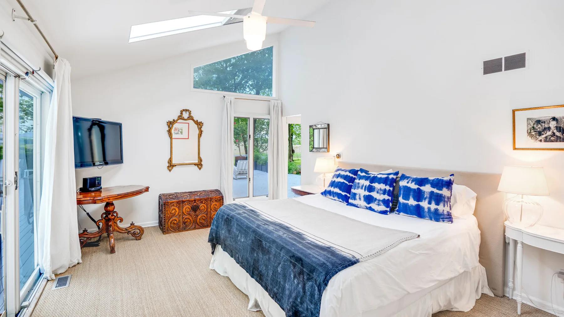 Un dormitorio luminoso con una cama vestida con ropa de cama blanca y azul.