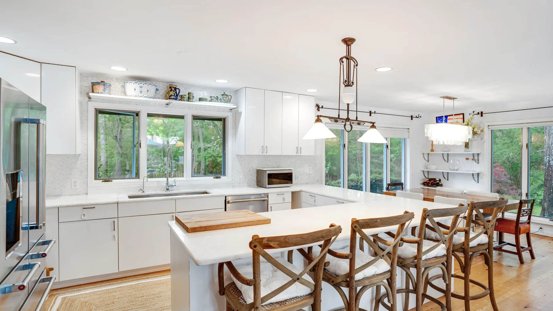 Una cocina luminosa con una isla grande y asientos de madera, rodeada de ventanas.