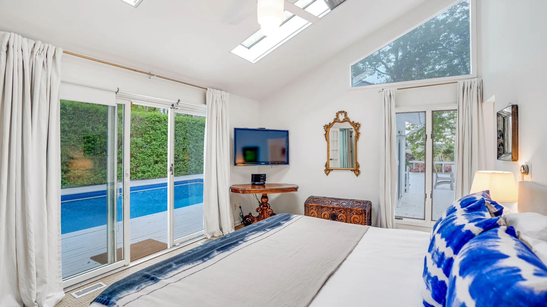 Un dormitorio luminoso con una cama frente a un televisor y puertas de vidrio junto a una piscina.