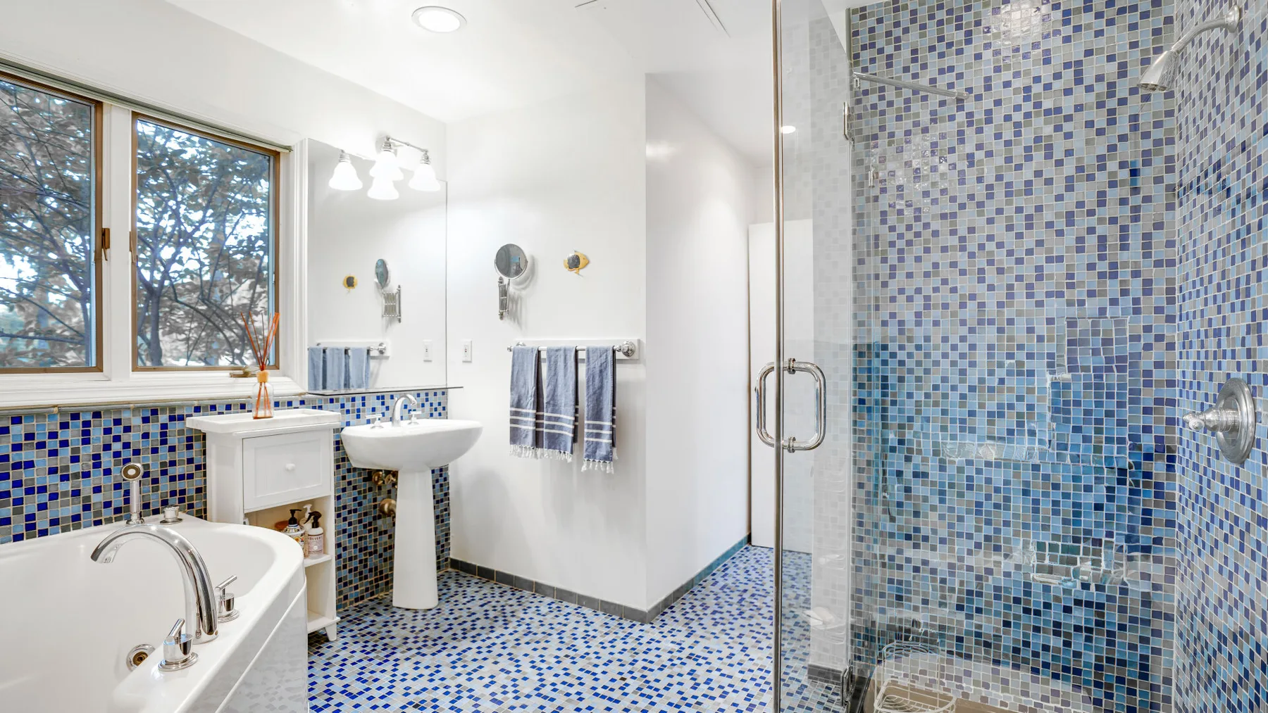Un baño luminoso con bañera, lavabo y mosaicos azules.