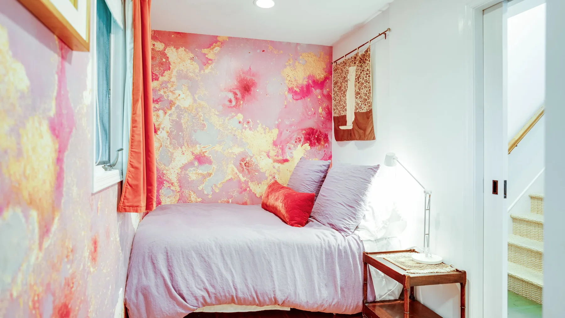 Un dormitorio con una cama, arte mural colorido y una pequeña mesa de noche.