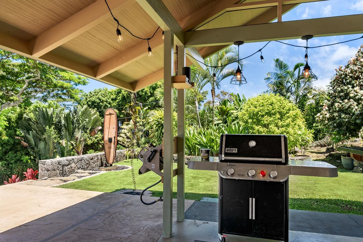 Una zona de cocina exterior cubierta con una parrilla frente a un jardín.