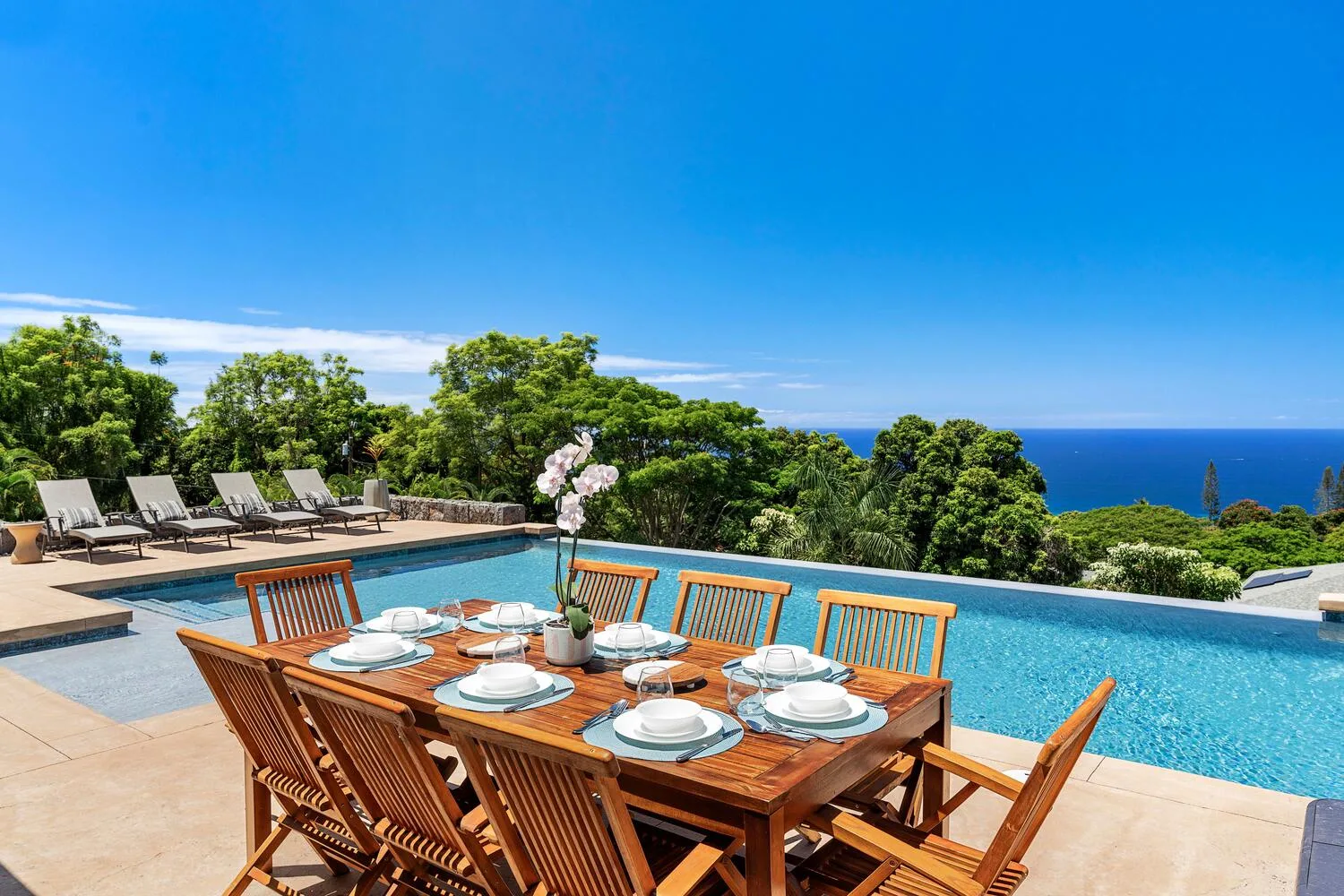 Una mesa de comedor al aire libre da a una piscina y al mar.